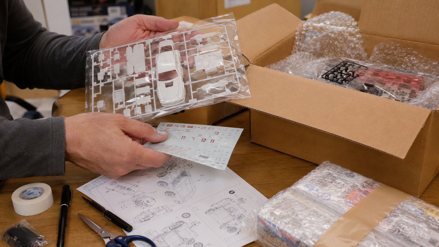 Scale model kit sprues, decals, instruction sheets, and packing materials being checked before shipping